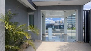 Edifici modern amb entrada de vidre, un camí de formigó i una palmera.