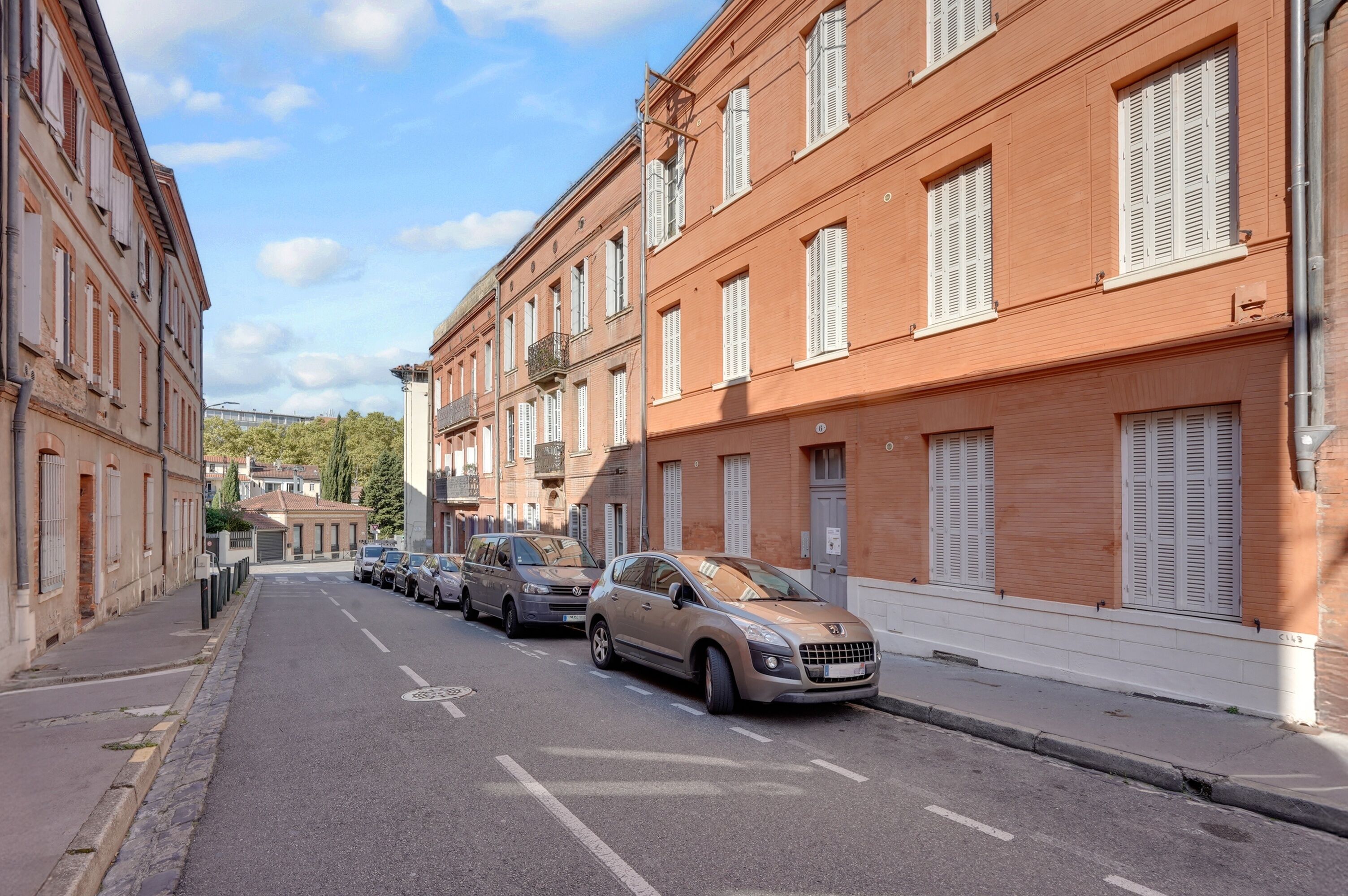 Carrer amb edificis, cotxes aparcats i cel serè.