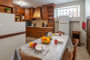 A kitchen with wooden cabinets, a stove, and a dining table set with plates, cups, and a fruit bowl. - La Maison du Bonheur - Grand Jardin (Coron)