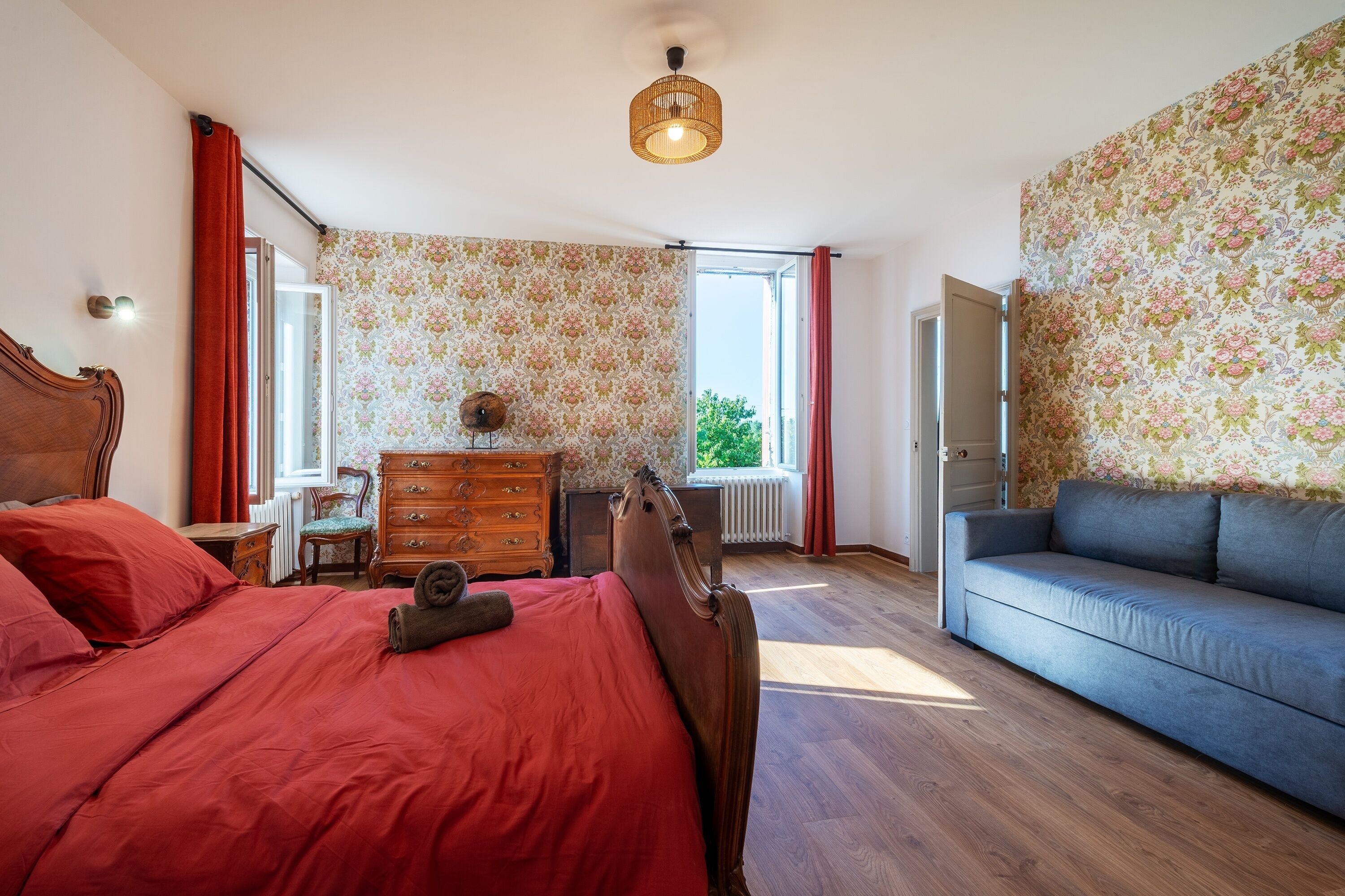 Une chambre à coucher avec un lit en bois, un canapé bleu, une commode et une fenêtre avec des rideaux.
