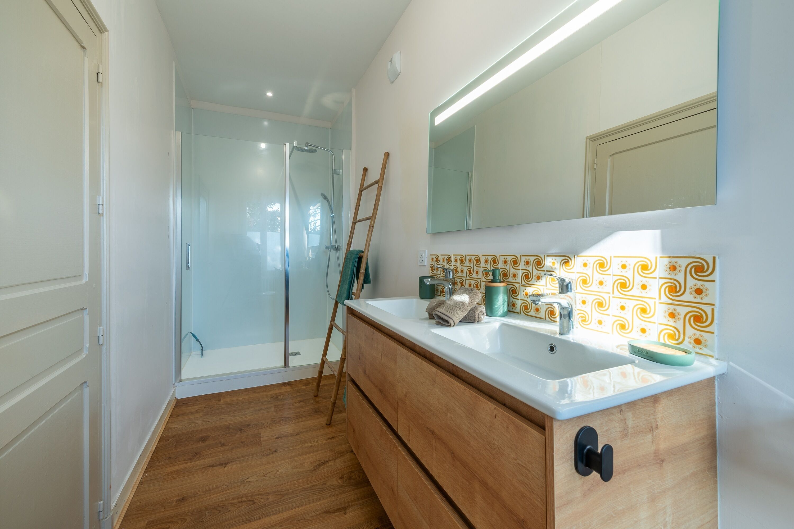 A bathroom with a wooden vanity, a glass shower enclosure, and patterned tiles.
