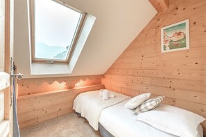 Ein Schlafzimmer mit schrägen Wänden, Holzboden und einem Oberlicht. Es gibt ein Bett mit weißer Bettwäsche und ein Poster an der Wand.