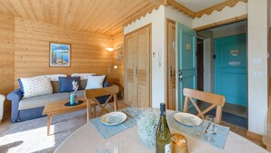 Un intérieur en bois comprenant un canapé, une table à manger et des chaises, un tableau accroché au mur et une porte avec une pancarte.