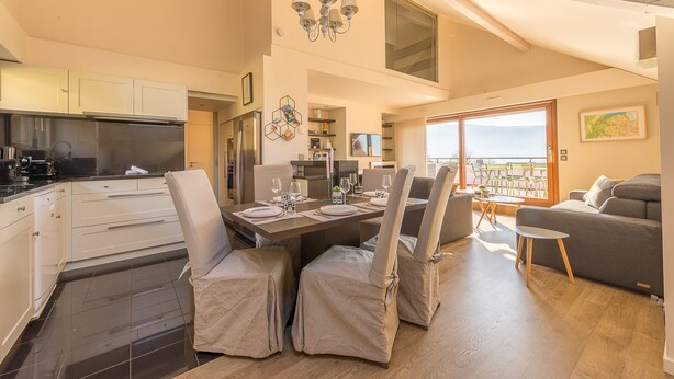 Una cocina moderna con armarios blancos, un comedor con mesa preparada para cuatro personas y un balcón con vistas.
