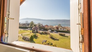 Vista a través de una ventana abierta de una zona residencial con casas, cielo despejado y una cadena montañosa distante.