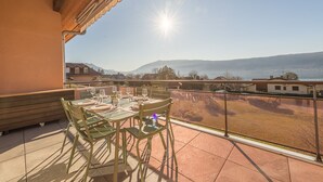 Un balcón con una mesa dispuesta para comer, con vistas a un paisaje pintoresco con montañas y cielo despejado.
