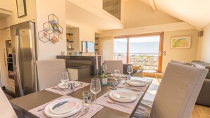 Un comedor con mesa preparada para cuatro, una cocina equipada con refrigerador y un balcón con vistas.