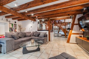 A modern living room with a sectional sofa, a glass coffee table, and exposed wooden beams.