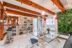 A modern interior with a glass dining table, bar stools, wooden beams, and a green wall.