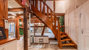 Una scala di legno in una stanza con pavimento piastrellato, una porta bianca e vista su un balcone con piante.