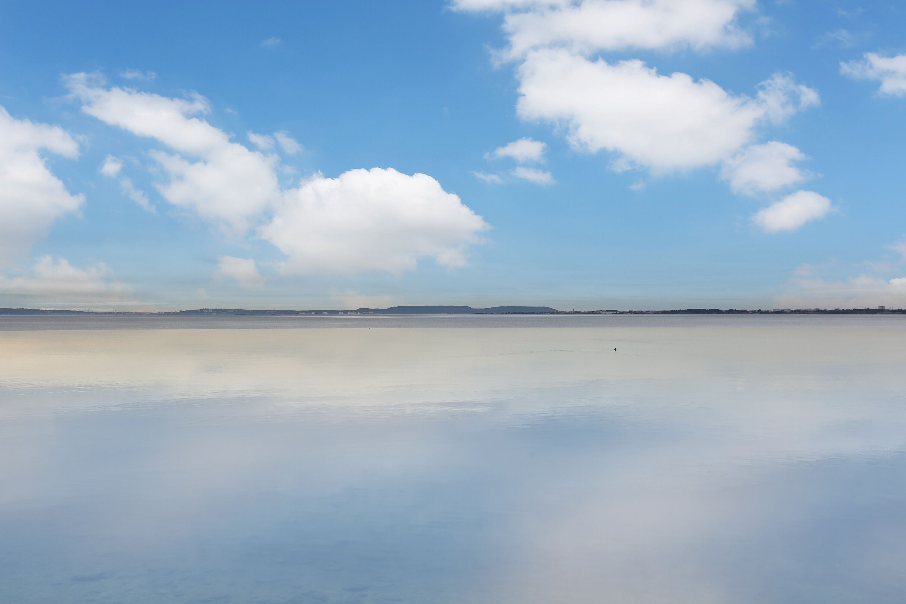 Una superficie acuática tranquila con cielo despejado y tierra lejana.