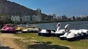 Uma área à beira do lago com embarcações, incluindo barcos em formato de cisne e bóias infláveis, atracadas perto de um calçadão pavimentado.