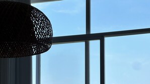 Uma área de refeições com uma mesa, cadeiras, um vaso com flores, uma luminária pendente texturizada e vista para a vegetação e uma montanha através de grandes janelas.