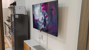 Et moderne køkken med køleskab, mikroovn og et fladskærms-tv ophængt på væggen.