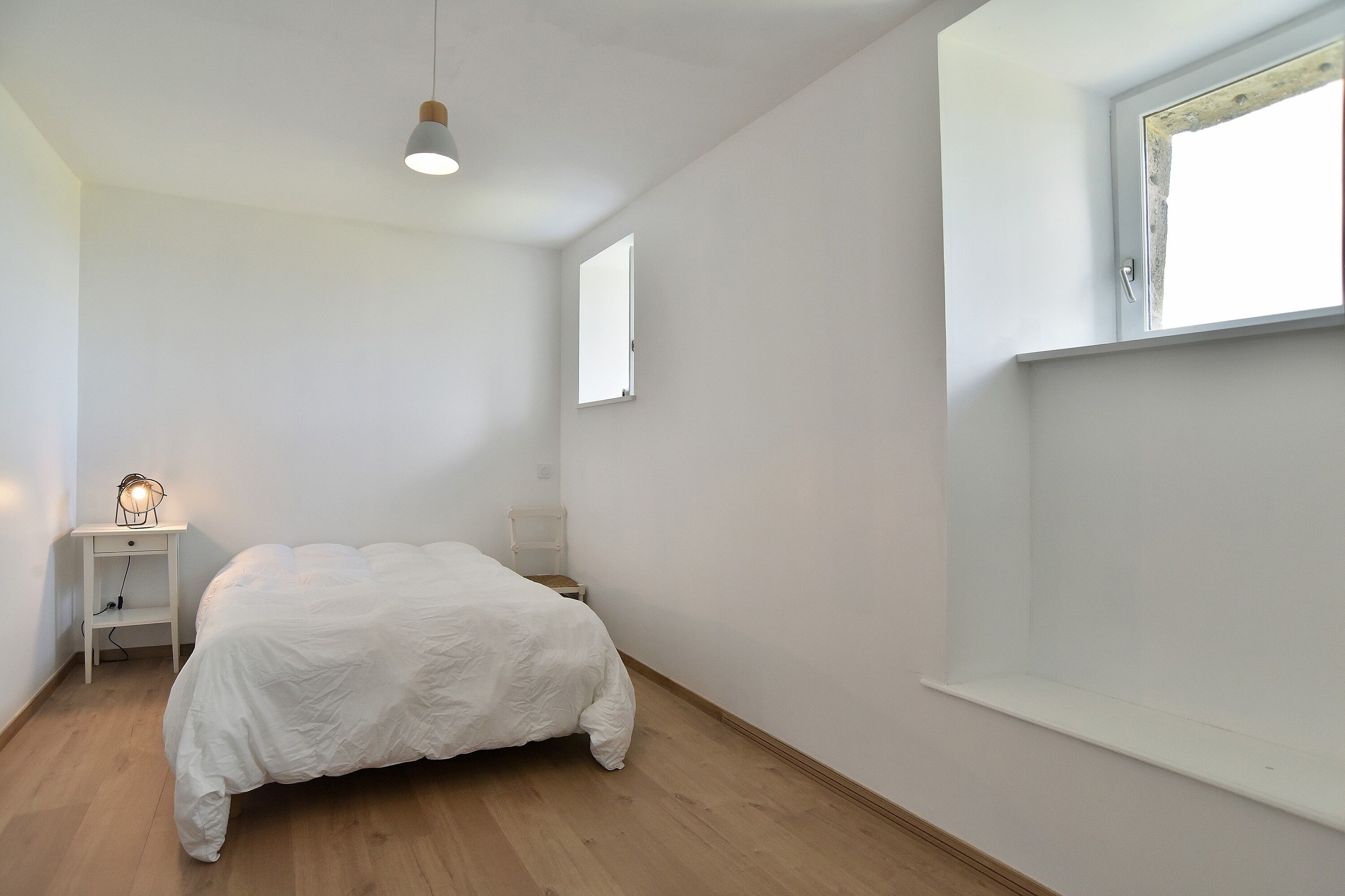 A bedroom with a bed, a nightstand, a lamp, a window, and a door.