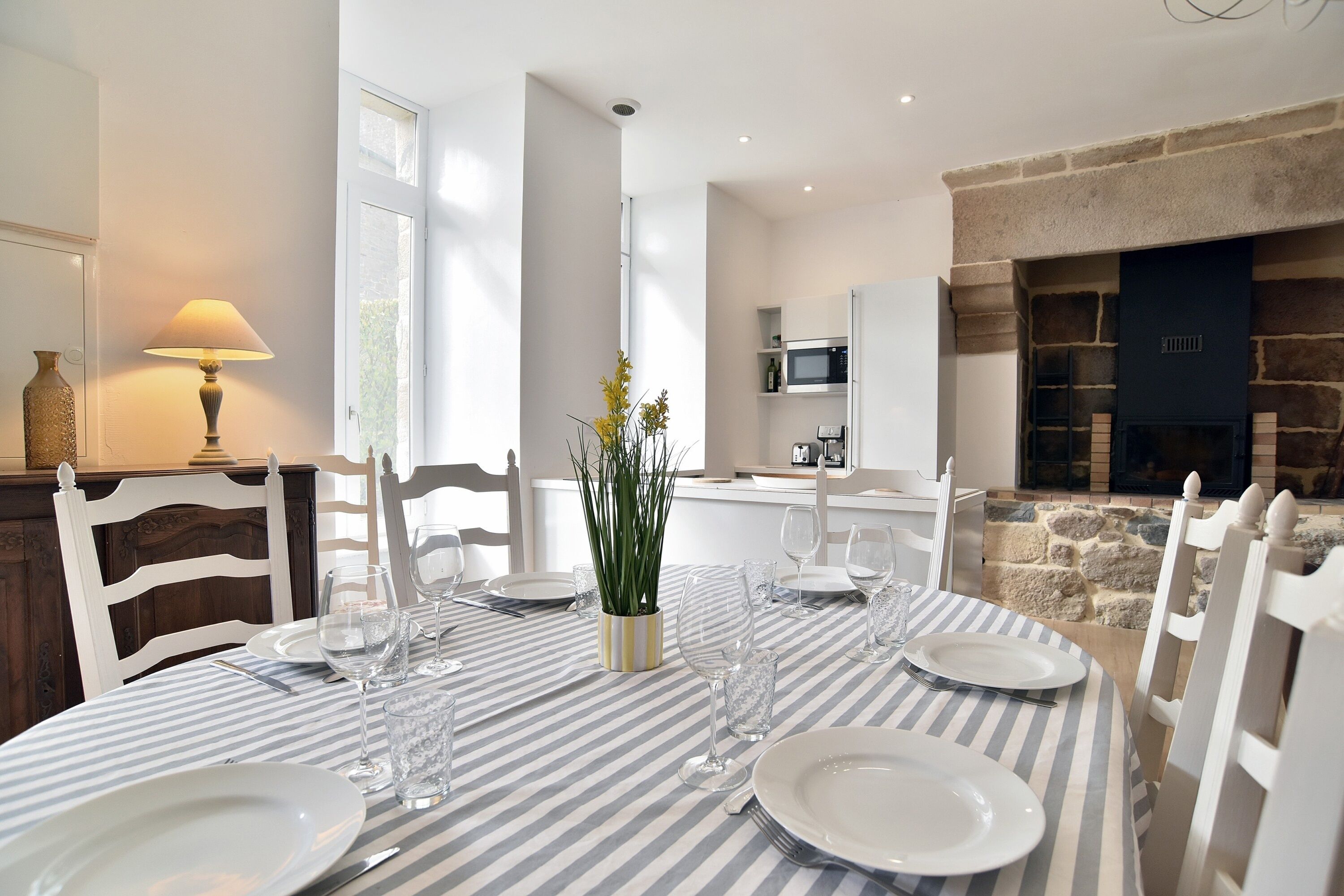 Un coin repas avec une nappe à rayures, des chaises blanches et une plante servant de centre de table.