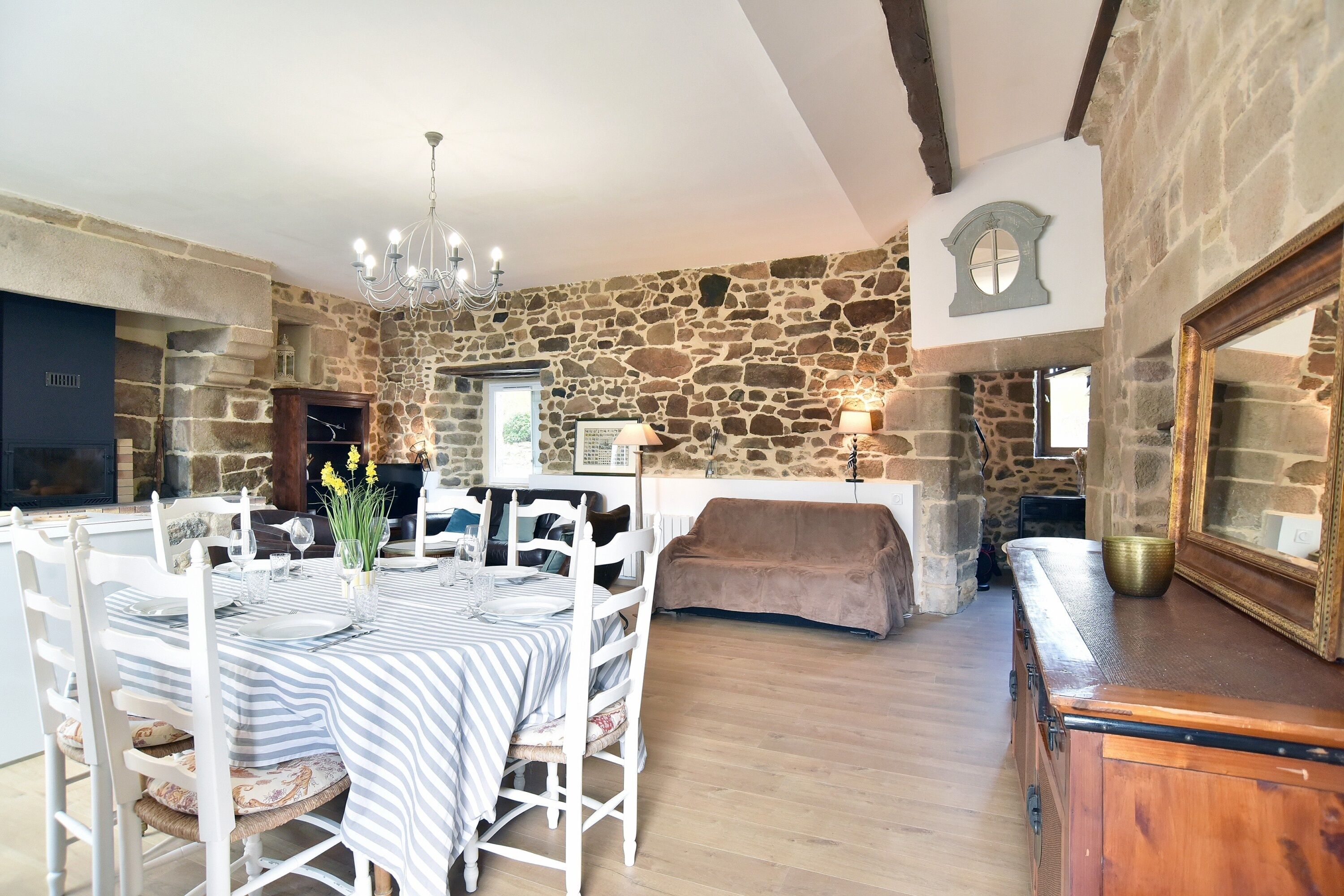 A stone-walled room with a dining table set for four, a fireplace, and a wooden cabinet.