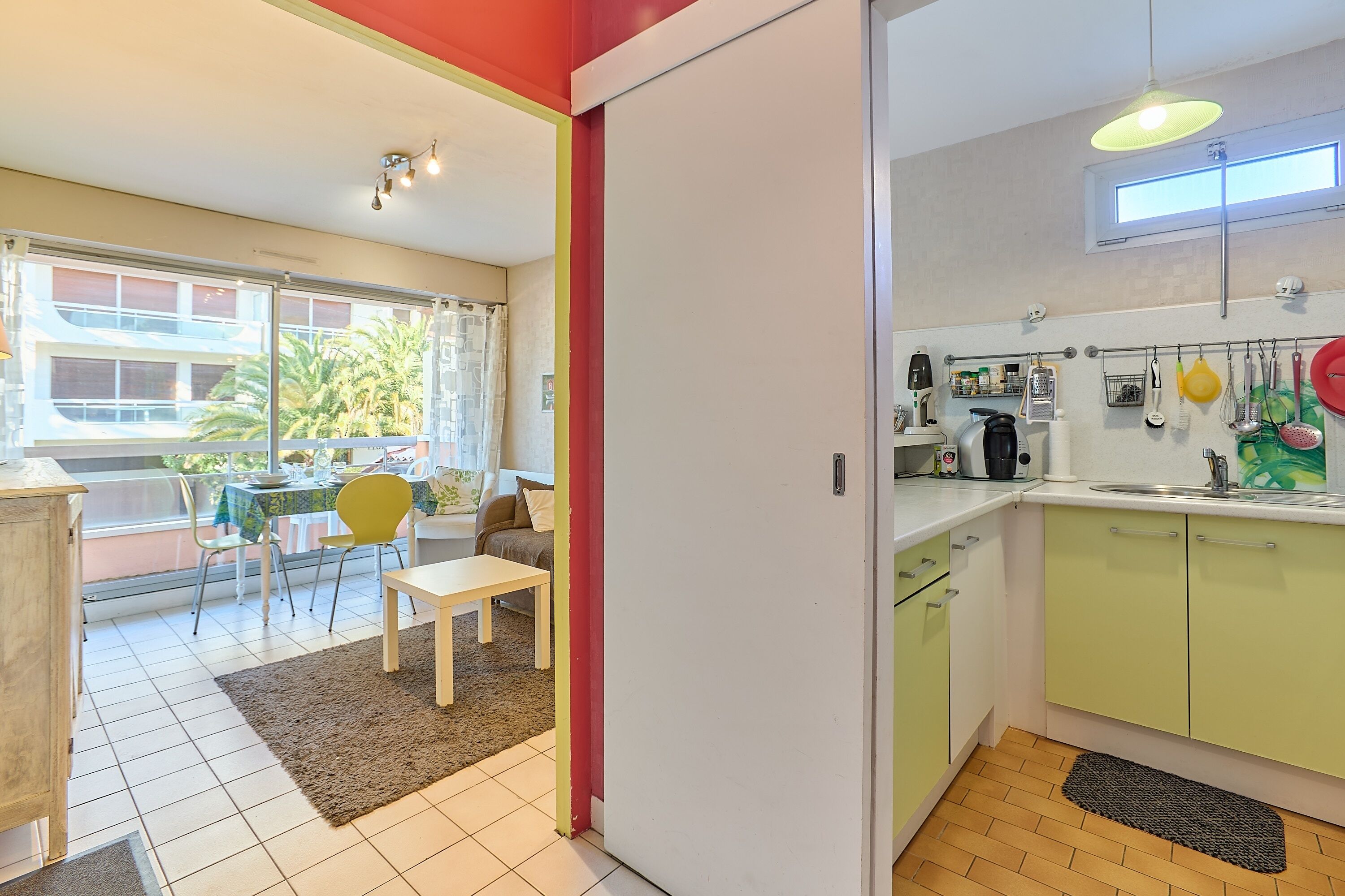 A kitchen with a window, a dining area with a table and chairs, and a view of a building outside.