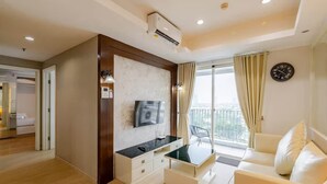 A modern living room with a flat-screen TV, a glass coffee table, a sofa, a balcony with curtains, and a clock on the wall. - Padi Suites Casa Grande, 2BR Apartment Mall Access (South Jakarta)