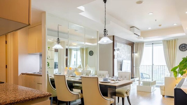 A modern living room with a dining area, wooden flooring, and a large window with curtains. - Padi Suites Casa Grande, 2BR Apartment Mall Access (South Jakarta)