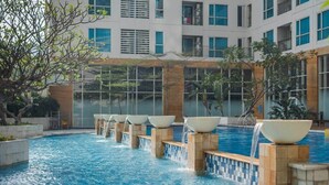 A swimming pool with multiple water features and a modern building in the background. - Padi Suites Casa Grande, 2BR Apartment Mall Access (South Jakarta)