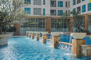 Ein Schwimmbecken mit mehreren Wasserspielen und einem modernen Gebäude im Hintergrund.