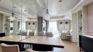 A modern hotel room with a large dining table, comfortable seating, a flat-screen TV, and a large mirror. - Padi Suites Casa Grande, 2BR Apartment Mall Access (South Jakarta)