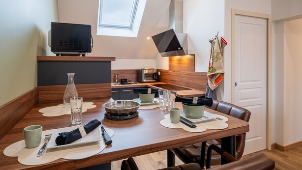 A modern kitchen with a dining table set for two, a television, and a window above the sink. - Le Tripot - A 15 min de la plage (Montebourg)