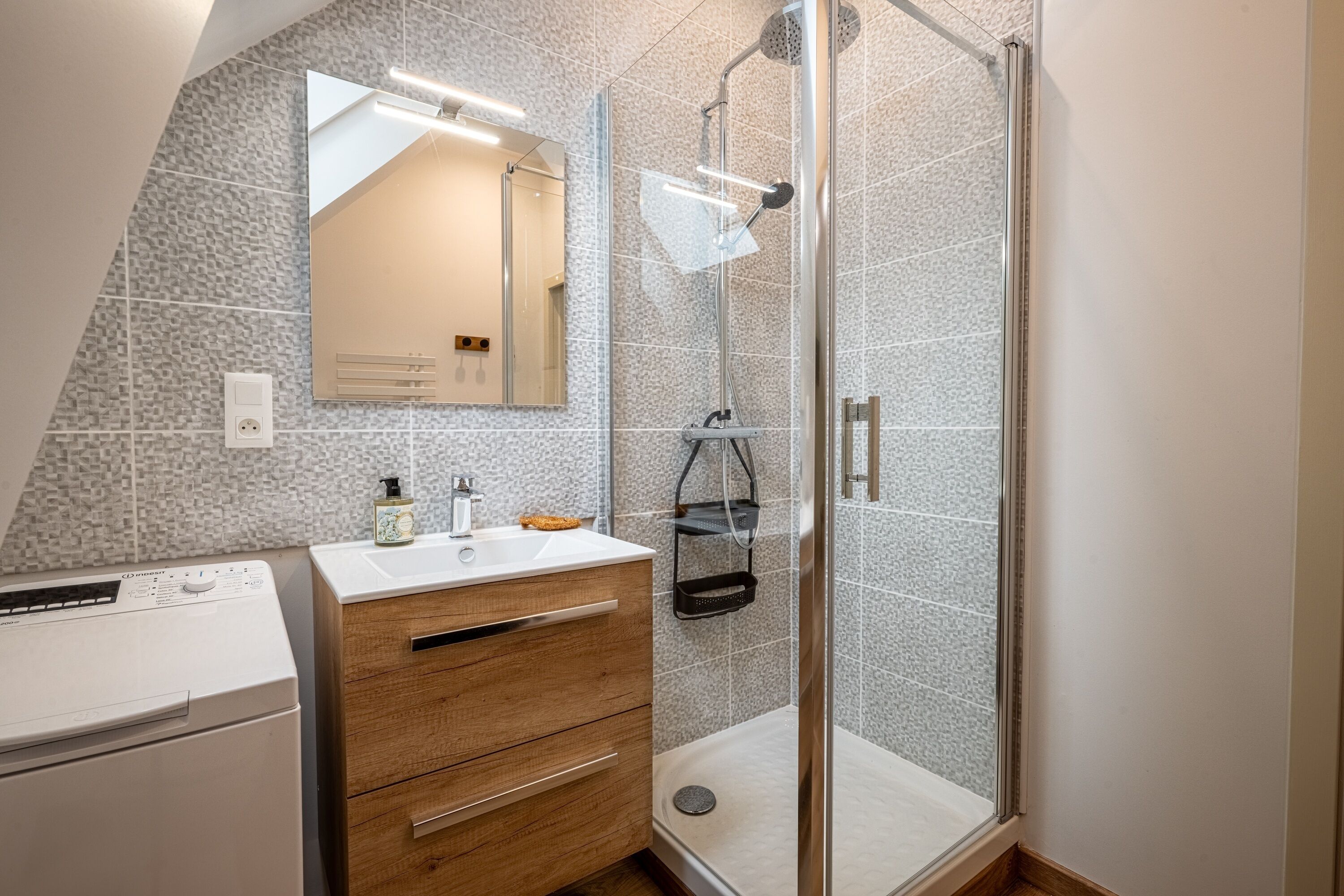 Un bagno moderno con box doccia in vetro, mobile lavabo in legno, lavatrice a incasso e uno specchio grande.