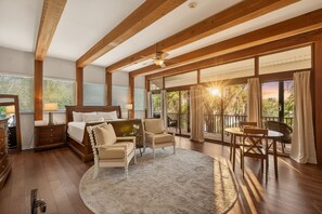 Ein Schlafzimmer mit einem Bett, zwei Stühlen, einem Tisch, einem Teppich, einem Deckenventilator und großen Fenstern mit Vorhängen.