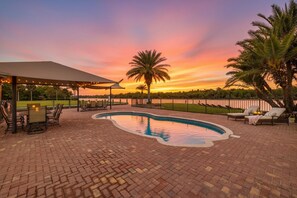 Un espace piscine offrant une vue sur le coucher de soleil, avec des sièges extérieurs et des palmiers.