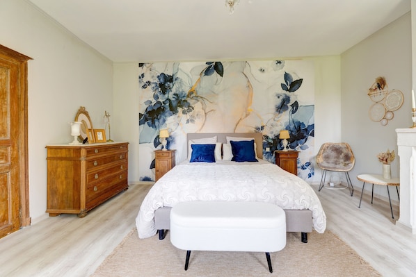 A bedroom with a large bed, a dresser, a chair, and a wall with a floral mural.