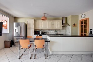 A modern kitchen with a central island, stainless steel appliances, and a dining area with orange chairs.