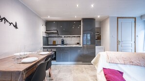 A compact kitchen with modern appliances, a dining area with a table set for two, and a bed with a single pillow. - La Belle Maurienne - Balcon avec vue sur montagne (Saint-Etienne-de-Cuines)