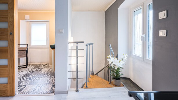 A hallway with a wooden floor, a metal railing, a potted plant, and a door leading to another room. - La Belle Maurienne - Balcon avec vue sur montagne (Saint-Etienne-de-Cuines)