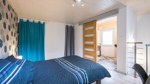 Une chambre à coucher comprenant un lit, une armoire, une chaise et une porte donnant sur une autre pièce.