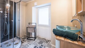 Une salle de bain avec une douche à parois de verre, un lavabo avec un récipient en verre, des carreaux de sol à motifs et un porte-serviettes.