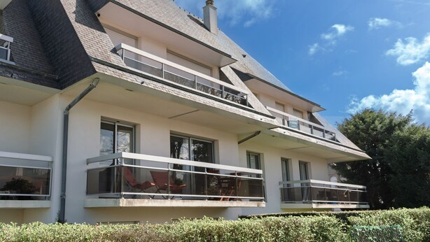 Ein zweigeschossiges Gebäude mit Balkon im zweiten Stock, einem Schornstein und blauem Himmel.