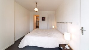 Ein Hotelzimmer mit Bett, Nachttischlampe, Tür und einem zur Toilette führenden Gang.