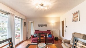 Ein modernes Wohnzimmer mit Esstisch, einem roten Sofa und einem großen Fenster mit Blick auf Gebäude.