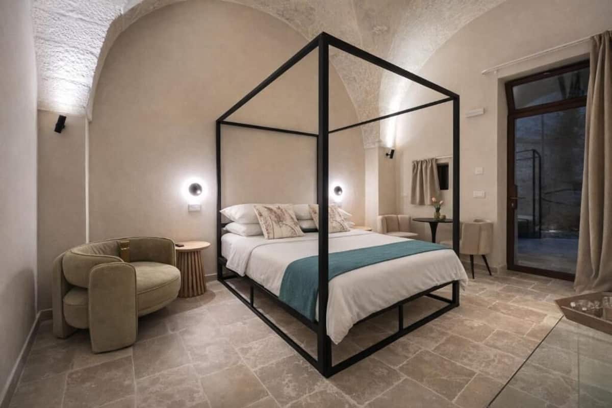 A modern bedroom with a four-poster bed, a round side table, a sofa, and a glass coffee table.