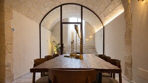 Una larga mesa de comedor con sillas, una escalera y una planta en una habitación con paredes de piedra.