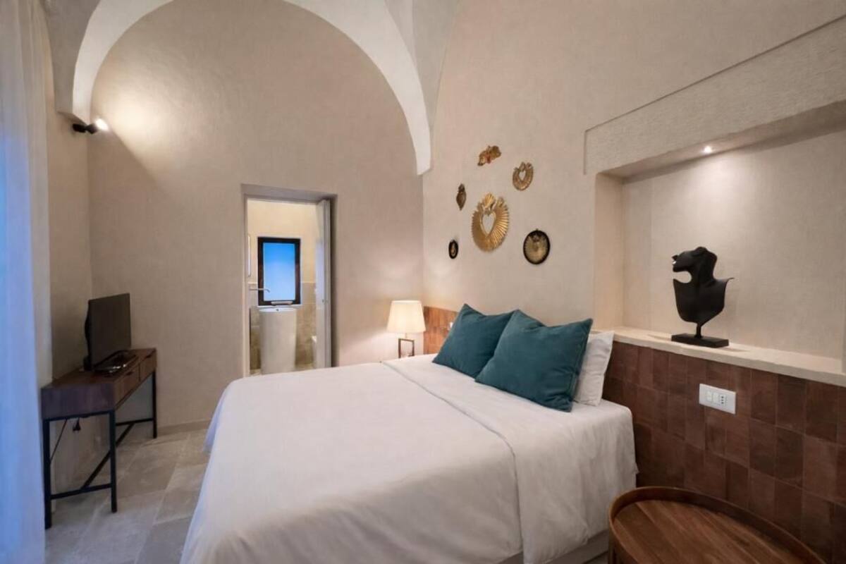 A hotel room with a bed, a desk, a TV, and a bathroom visible through an arched doorway.