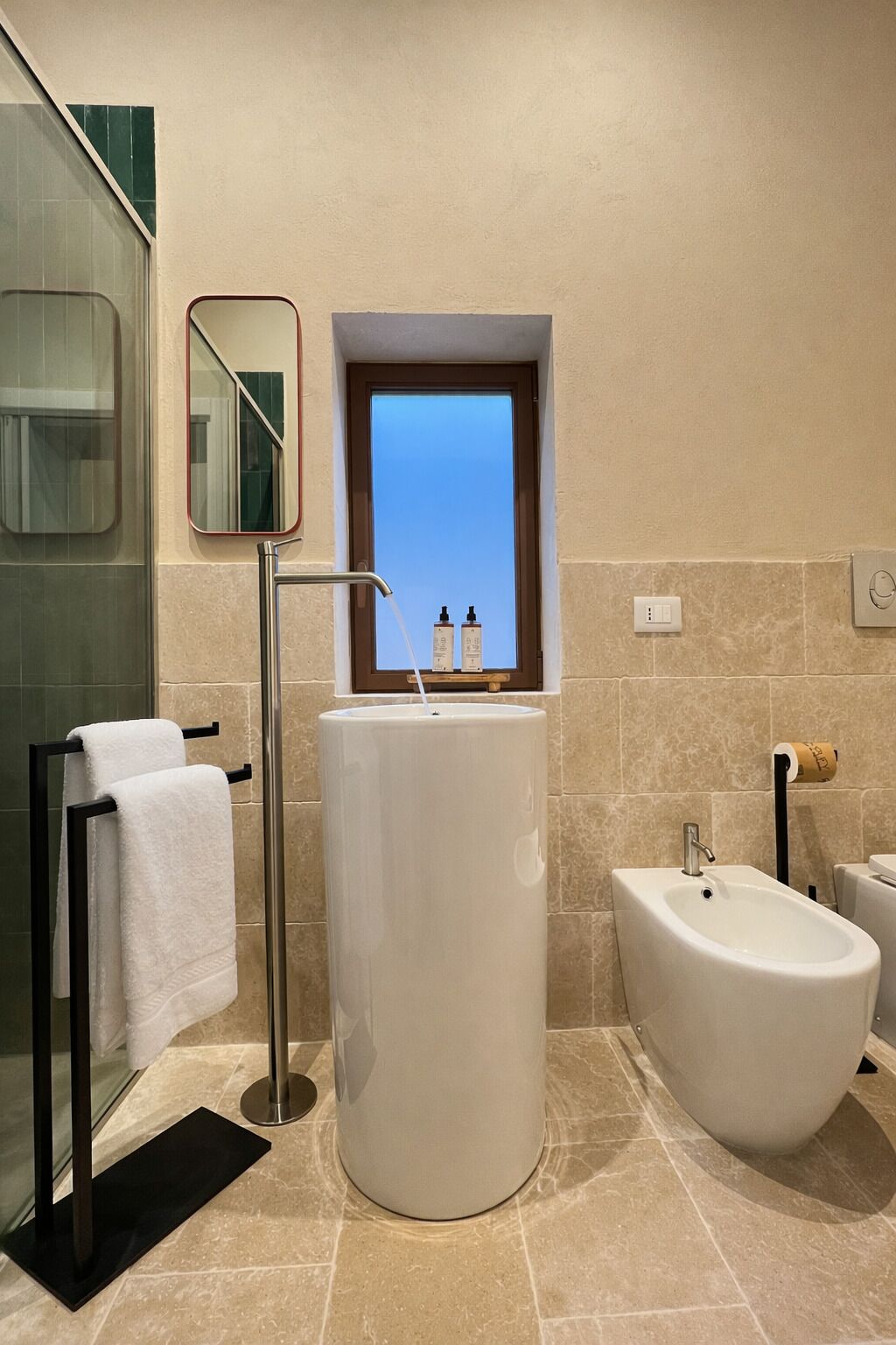 Ein modernes Badezimmer mit freistehender Badewanne, einem großen Spiegel und einem Fenster mit Ausblick.