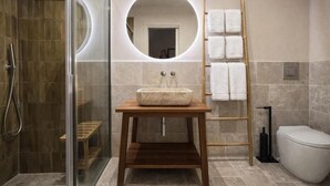 Un baño con ducha de vidrio, tocador de madera con lavabo de mármol, un espejo redondo y un perchero para toallas.