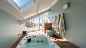 Un jacuzzi en una habitación con tragaluces, suelo de madera y vistas al exterior.