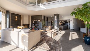 Un amplio salón con techo alto, un sofá grande, una mesa de centro, chimenea, estantería y zona de comedor.