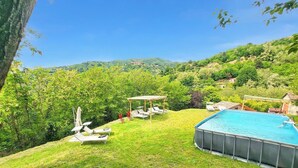 Une piscine, des chaises longues et un kiosque au milieu d’un paysage verdoyant et luxuriant.