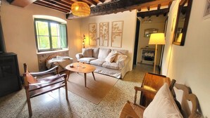 Un salon chaleureux avec un canapé, des fauteuils en bois, une table basse, une cheminée et une fenêtre avec des rideaux.