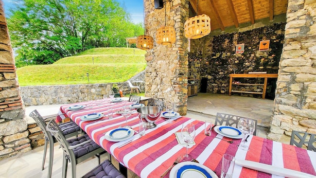 Un espace de restauration en plein air, avec un mur en pierre, une table dressée avec des assiettes, des verres et des couverts, et des lanternes suspendues.